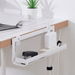"The image shows an IKEA FÖRSÄSONG cable management tray in white, measuring 38 cm, attached to the edge of a desk. The tray is designed to organize and manage cables and small electronic devices. In the tray, there is a white power adapter plugged into a power strip and a black stapler. The desk has a white tiled surface with a wooden edge, and there is a laptop with a charging cable connected to it. Additionally, there are two small potted plants on the desk, adding a touch of greenery to the workspace. 