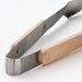 Close-up of tongs: "Durable stainless steel and beech wood barbecue tongs for precise and stylish grilling