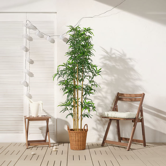 Tall FEJKA bamboo plant in woven basket beside green sofa and wooden chairs