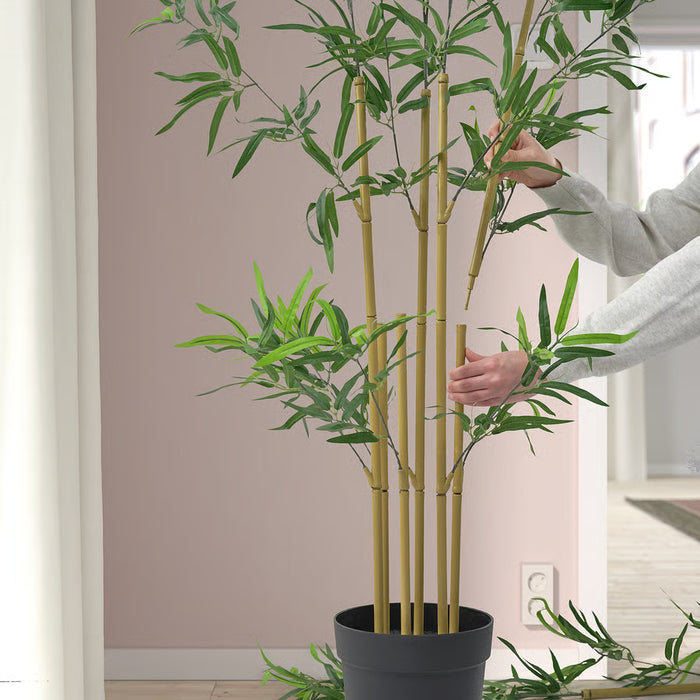 Hands arranging FEJKA bamboo plant showing green leaves and yellow stalks