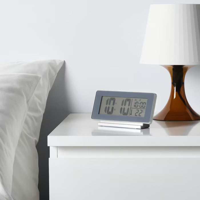  IKEA FILMIS grey alarm clock on bedside table with lamp, displaying time, temperature and snooze function