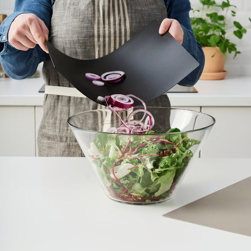 Person bending IKEA FINFÖRDELA chopping board to slide chopped onions into a salad bowl