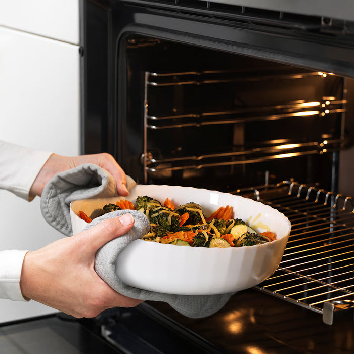 Fresh vegetables being sliced beside IKEA FISKTÄRNA white glass oven dish on cutting board