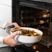 Fresh vegetables being sliced beside IKEA FISKTÄRNA white glass oven dish on cutting board