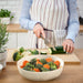 Hands in oven mitts carrying IKEA FISKTÄRNA glass dish with vegetables into open oven