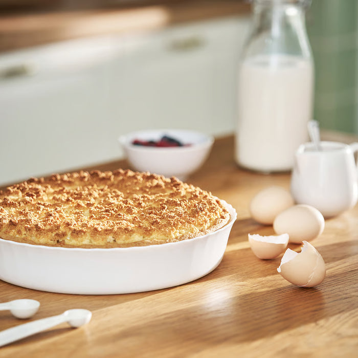 Baked dish in IKEA FISKTÄRNA white ceramic pie plate surrounded by eggs milk and berries
