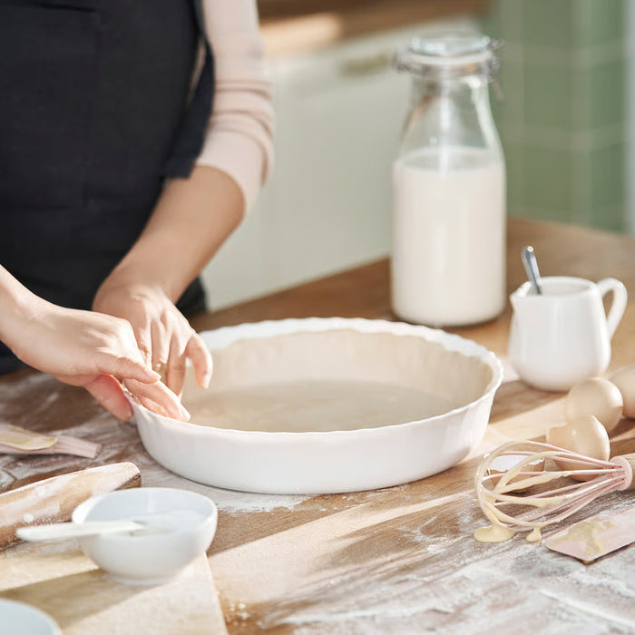 Person preparing pie dough in IKEA FISKTÄRNA white dish on floured wooden table