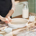 Person preparing pie dough in IKEA FISKTÄRNA white dish on floured wooden table