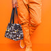 Person in grey hoodie opening IKEA FLADDRIG patterned lunch bag seated casual setting