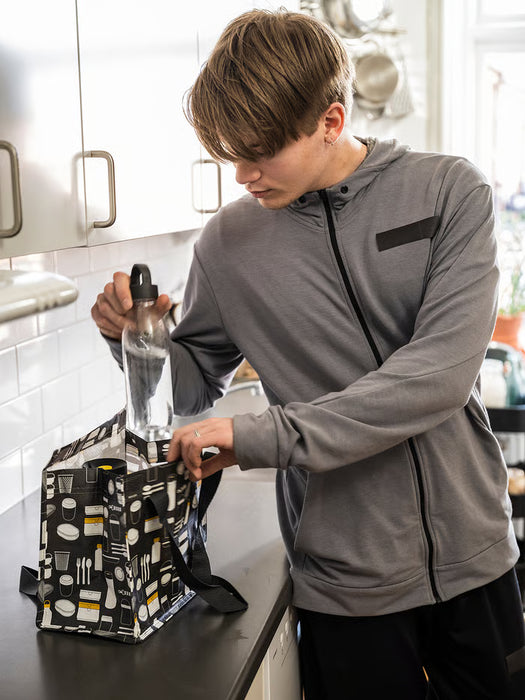 Person on pier unpacking IKEA FLADDRIG grey patterned lunch bag outdoors by the ocean