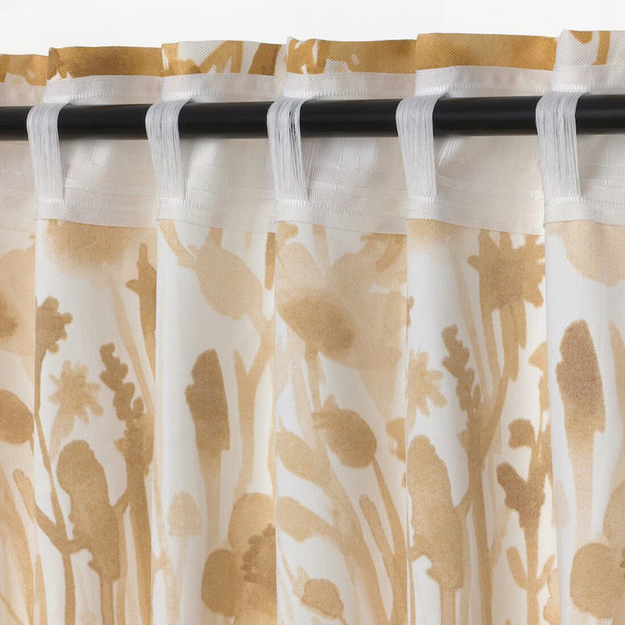 A close-up view of IKEA FLENTIMOTEJ curtains, featuring a light beige color with a floral pattern. The curtains measure 145x250 cm and are hung on a curtain rod, displaying the semi-sheer fabric and the tab tops that allow for easy hanging. The pattern consists of abstract floral shapes in a slightly darker beige tone, providing a subtle yet elegant design suitable for various interior decors.