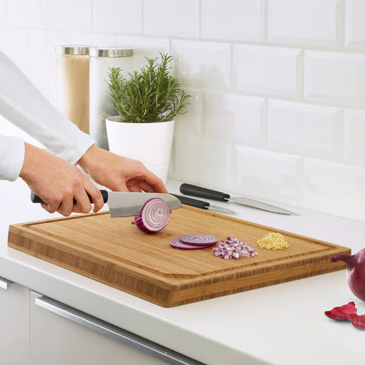 IKEA FÖRSLAG cook's knife slicing red onion on wooden cutting board, two knives resting on white countertop