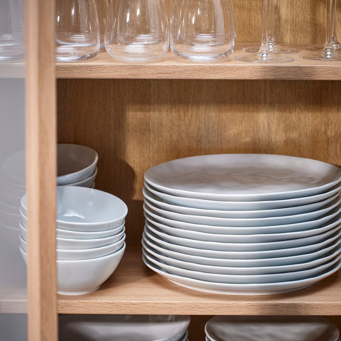 Stacks of IKEA FORELLTETRA white porcelain plates and bowls on shelves with clear glassware