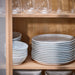 Stacks of IKEA FORELLTETRA white porcelain plates and bowls on shelves with clear glassware