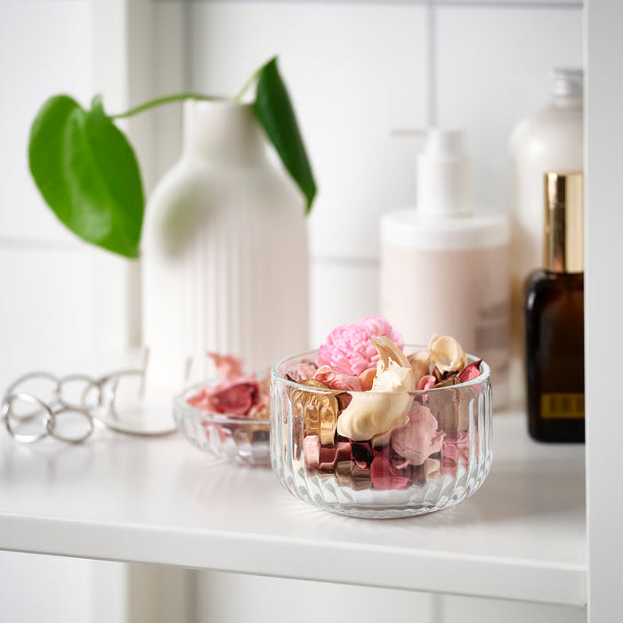 Glass bowl of IKEA FRÖFINK potpourri styled with plants and bottles on a white shelf