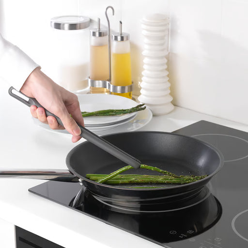 IKEA FULLÄNDAD grey cooking tweezers turning asparagus in black non-stick frying pan on modern stove