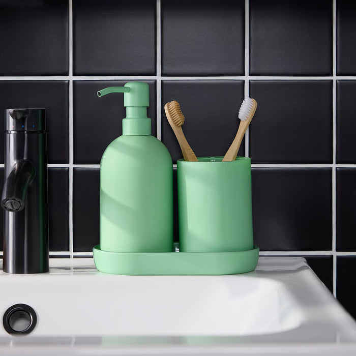 Green bathroom set with soap dispenser, toothbrush holder, and toothbrushes on a black tiled wall background.