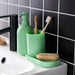 Green bathroom accessories including a soap dispenser, toothbrush holder, and scrub brush on a sink.