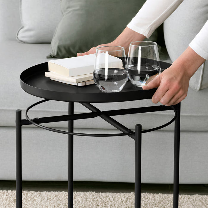 Person serving wine glasses on IKEA GLADOM black tray table with books alongside sofa