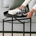Person serving wine glasses on IKEA GLADOM black tray table with books alongside sofa