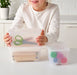 Hand holding open IKEA GLIS pink turquoise plastic box with lid containing scissors and pencils