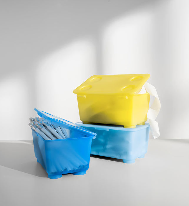 IKEA GLIS yellow and blue boxes with lids stacked containing pens and pencils on white surface
