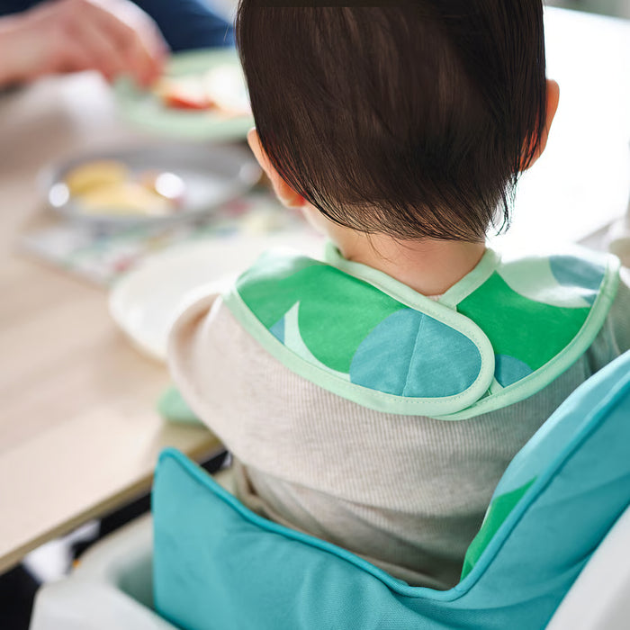 Child in high chair wearing IKEA GRÖNFINK green bib with front pocket catching food during mealtime