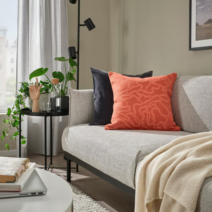 Living room with a gray sofa featuring orange and black patterned cushions, a small round table with plants, and a lamp.