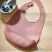 Soft pale pink IKEA GULDVÄVARE baby feeding bib with crumb-catching pocket and adjustable snap closure, made of easy-clean polyester for mess-free mealtimes.


