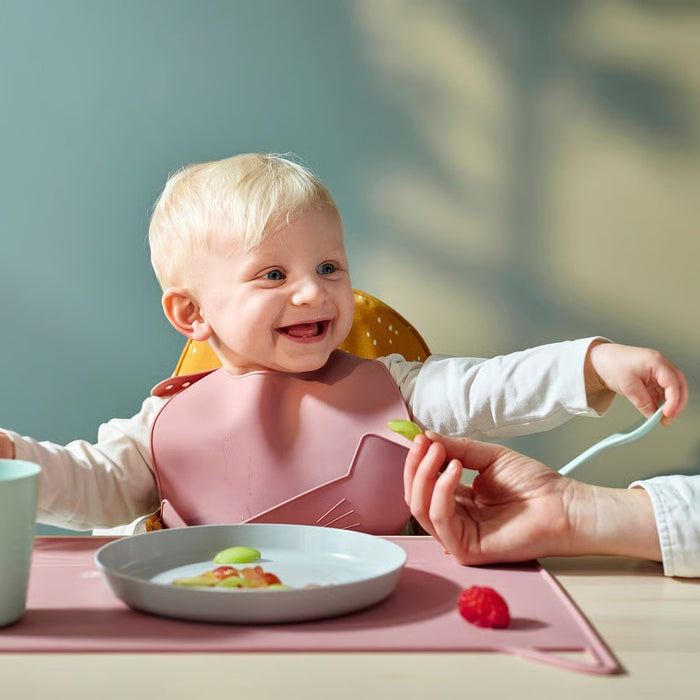 IKEA GULDVÄVARE infant bib in delicate pale pink featuring a deep food-catching pocket and comfortable neck sizing, machine-washable for convenient reuse.

