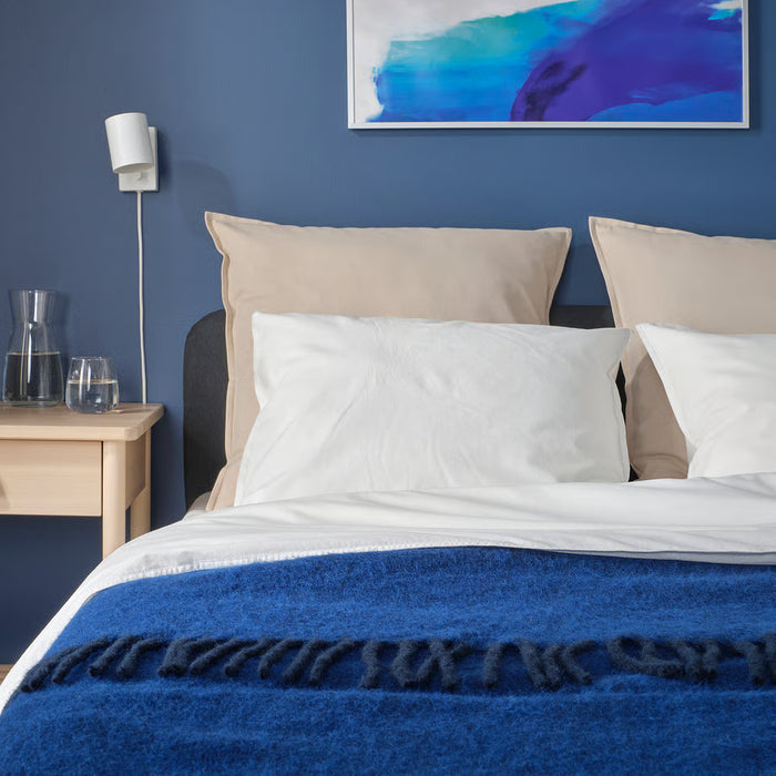Large IKEA GURLI unbleached cushion covers on a bed with a blue blanket and wooden bedside table