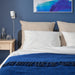 Large IKEA GURLI unbleached cushion covers on a bed with a blue blanket and wooden bedside table