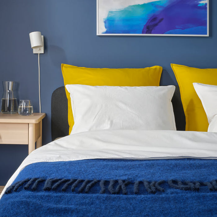 IKEA GURLI yellow cushion on a bed in a bedroom with blue walls and abstract wall art