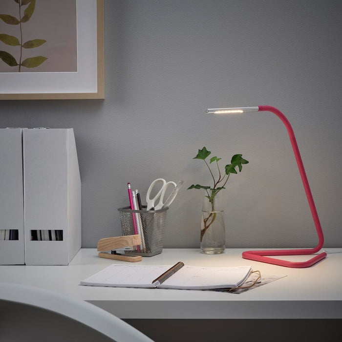 IKEA HÅRTE LED work lamp in use on a desk, providing vibrant pink lighting with a silver touch, ideal for workspaces-00507594