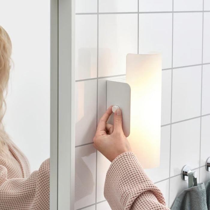 Person adjusting a wall-mounted light fixture in a bathroom.