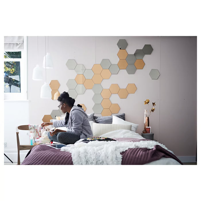 Cosy bedroom with person reading on bed and IKEA HÖNEFOSS hexagon mirrors displayed on wall