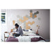 Cosy bedroom with person reading on bed and IKEA HÖNEFOSS hexagon mirrors displayed on wall