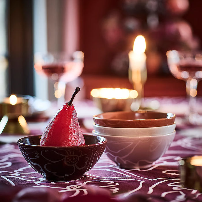 IKEA HÖSTAGILLE stacked bowls beside a small patterned bowl holding a dark red pear on a floral tablecloth