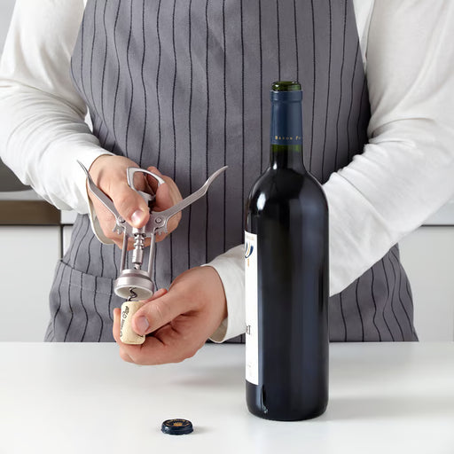 Person using IKEA IDEALISK corkscrew to remove cork from wine bottle effortless lever action