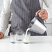 Person pouring liquid from IKEA IDEALISK stainless steel measuring jug showing dl and pint graduation markings