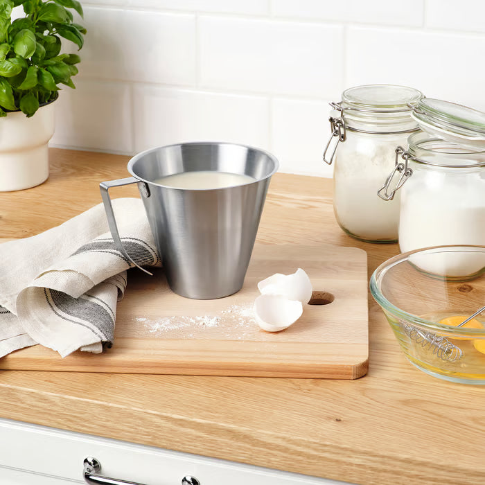 KEA IDEALISK stainless steel measuring jug on wooden cutting board with baking ingredients and kitchen tools