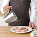 IKEA IDEALISK stainless steel jug being used to pour sauce over chocolate dessert on a plate
