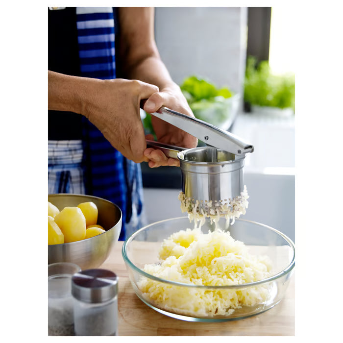Close-up of the IKEA IDEALISK potato press basket and handle, showing the polished stainless steel finish and hole pattern