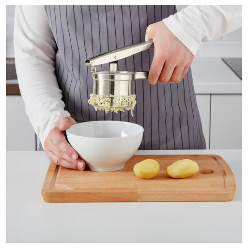 IKEA IDEALISK potato press in use, pressing boiled potatoes into a silver pot, showing creamy mashed potato texture