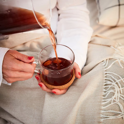 Person pouring drink into glass mug placed on IKEA 365+ cork coaster on table