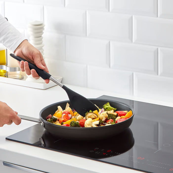 IKEA 365+ HJÄLTE black spatula being used to cook colourful vegetables in a non-stick pan on an induction stovetop