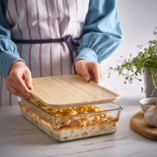 Person placing IKEA 365+ bamboo lid on glass baking dish with lasagna for fridge storage