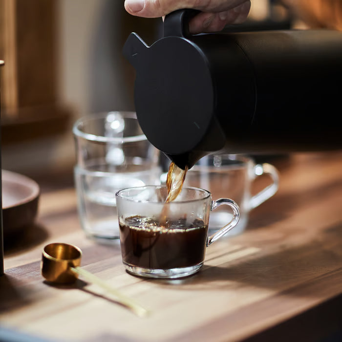 Person pouring coffee into IKEA 365+ clear glass mug on a wooden table
