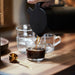Person pouring coffee into IKEA 365+ clear glass mug on a wooden table