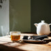 IKEA 365+ glass mug filled with steaming tea on wooden table next to white teapot and silver spoon